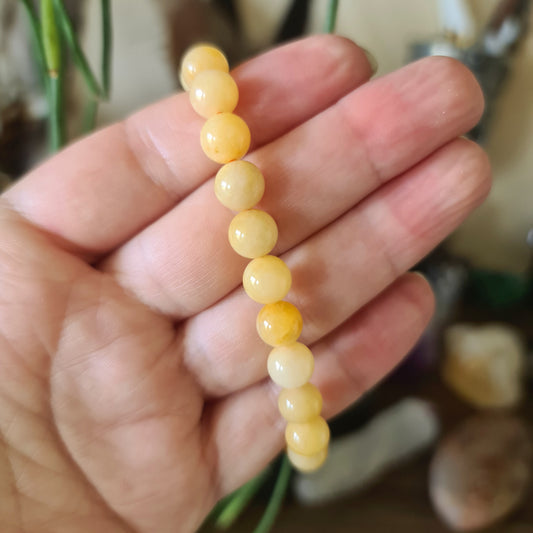 A person holding a yellow jade bracelet with a smooth, polished finish.