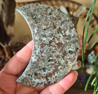 A polished crescent-shaped stone with a brown and gray marbled pattern, held in a person's hand.