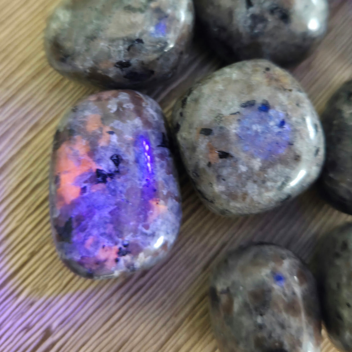 Rounded tumbling stones with a smooth surface, displaying a mix of colors including blue and pink, on a wooden background.