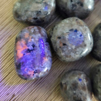 Rounded tumbling stones with a smooth surface, displaying a mix of colors including blue and pink, on a wooden background.