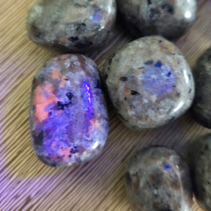 Rounded tumbling stones with a smooth surface, displaying a mix of colors including blue and pink, on a wooden background.