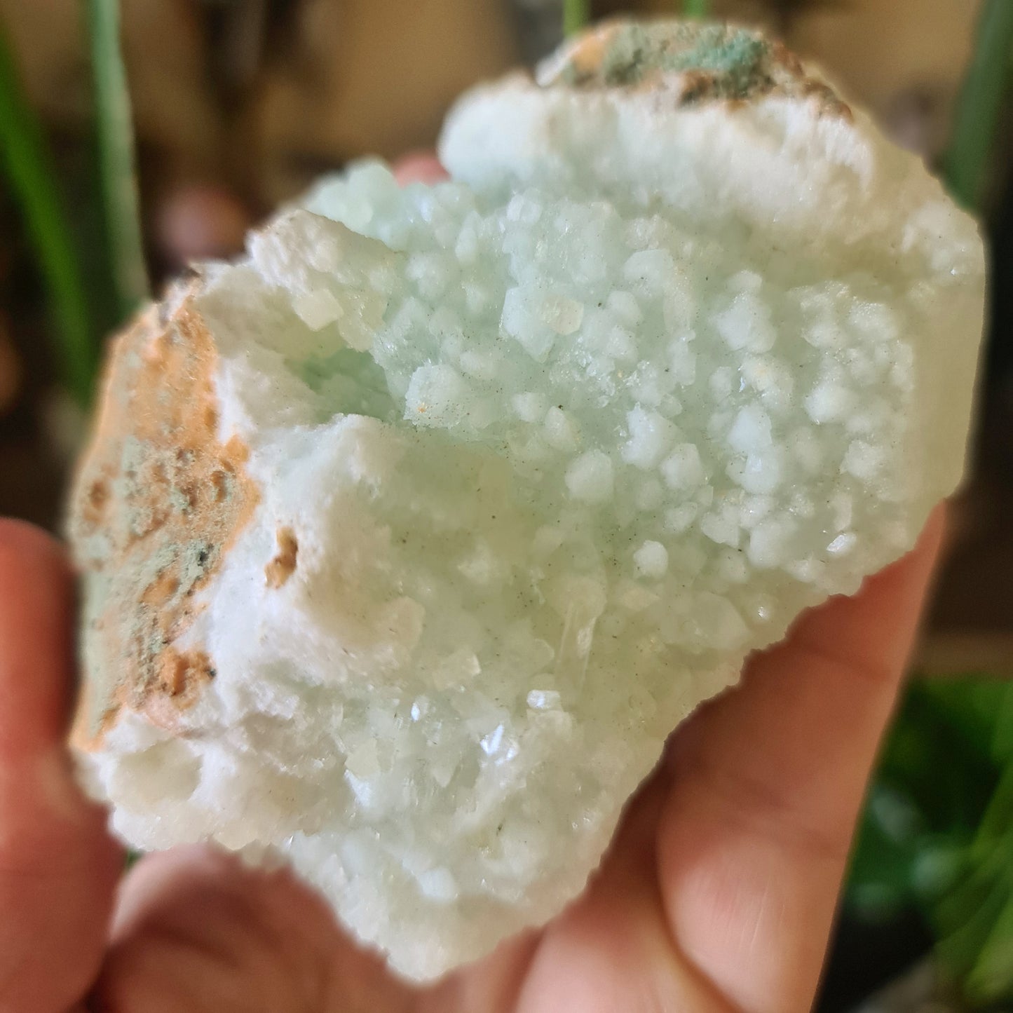A hand holding a zeolite crystal cluster with a blue-green color and a rough, textured surface.