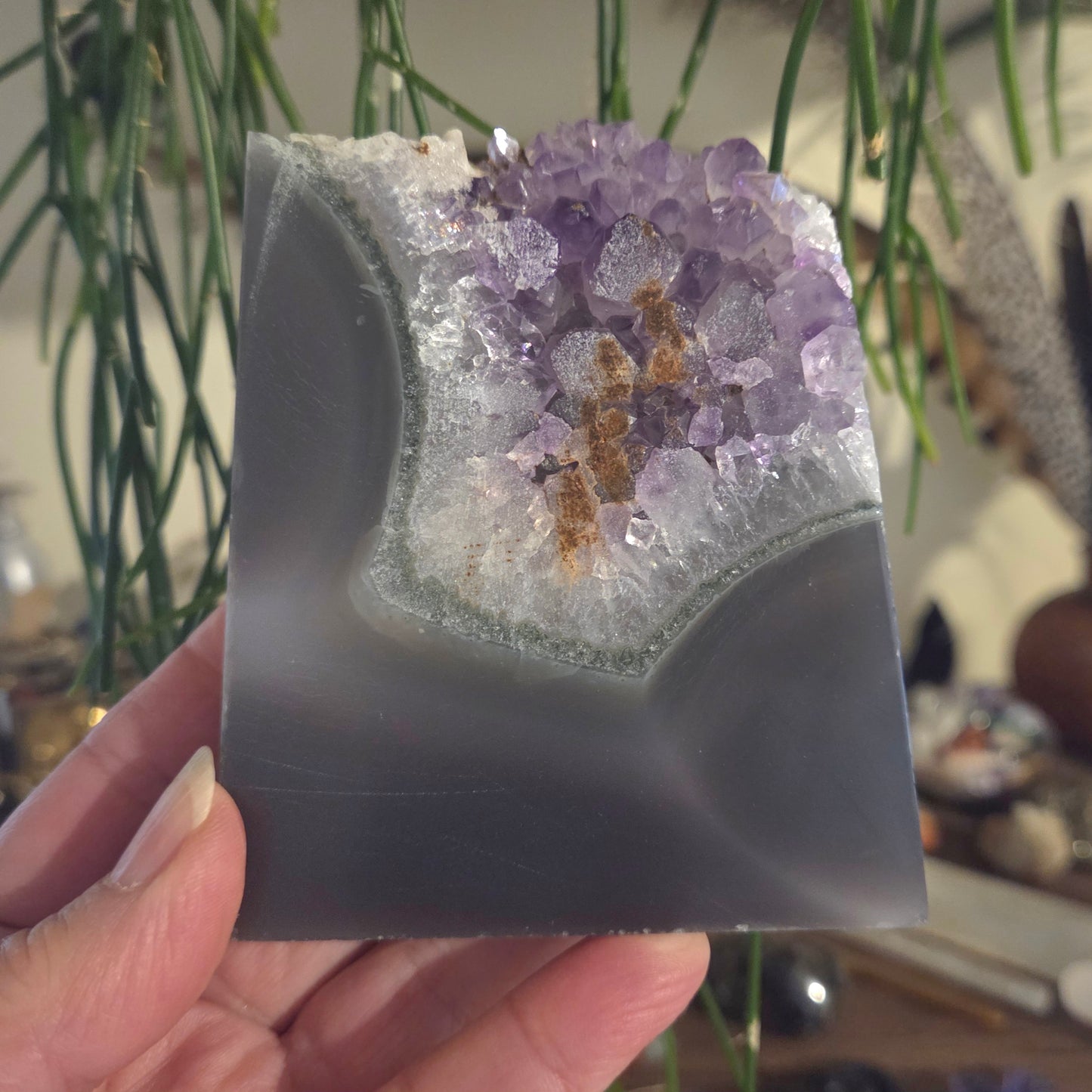 Amethyst crystal geode held by a hand with a blurred indoor background