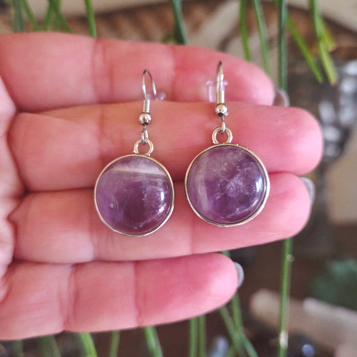Purple gemstone earrings held in a hand with a blurred natural background