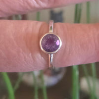 Silver ring with a purple gemstone on a finger against a blurred green background