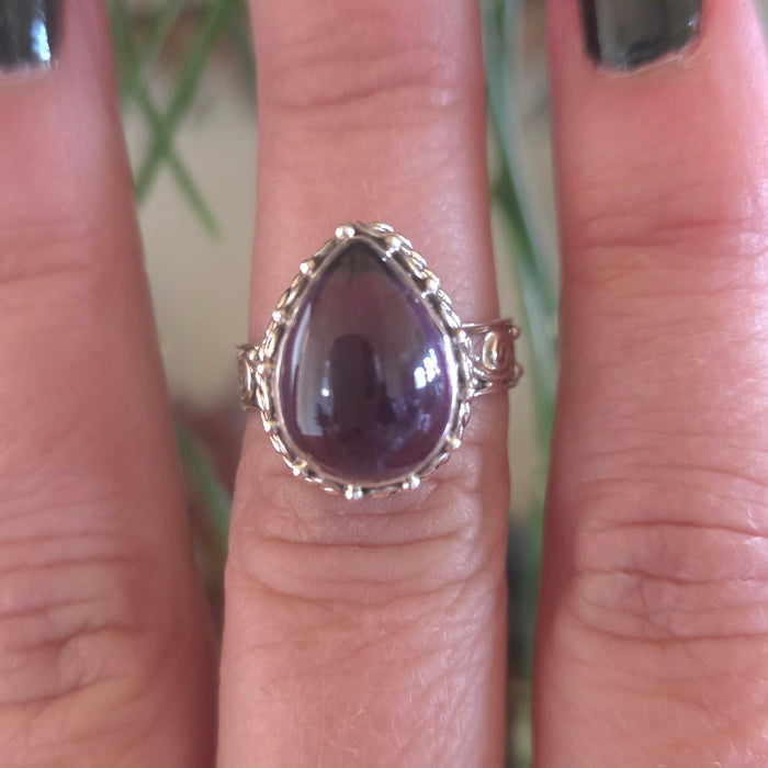 Ring with a purple stone on a finger against a blurred natural background