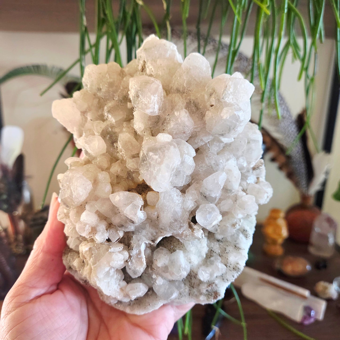 Hand holding a large crystal cluster with a blurred indoor background
