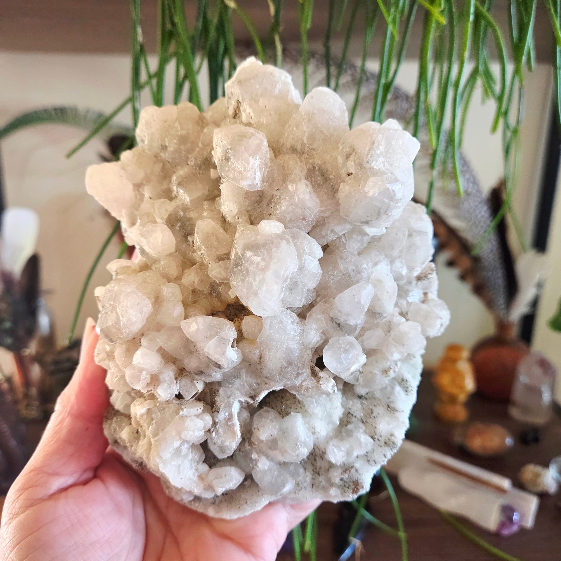 Hand holding a large crystal cluster with a blurred indoor background
