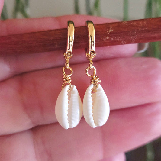 Gold earrings with shell drops held against a hand.