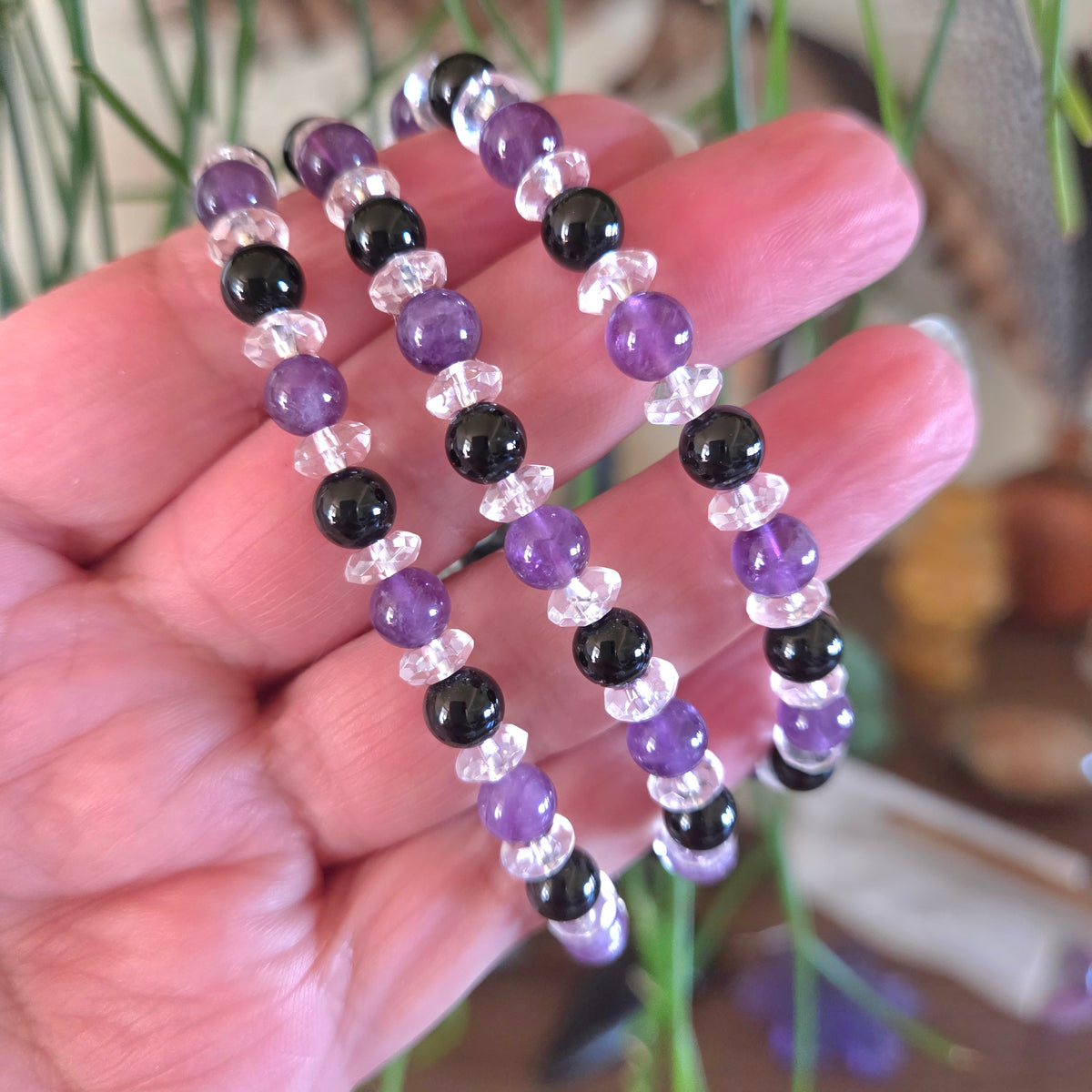 Hand holding a set of beaded bracelets with purple, black, and clear beads.