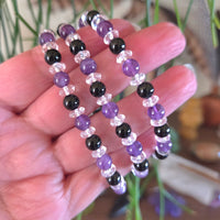 Hand holding a set of beaded bracelets with purple, black, and clear beads.