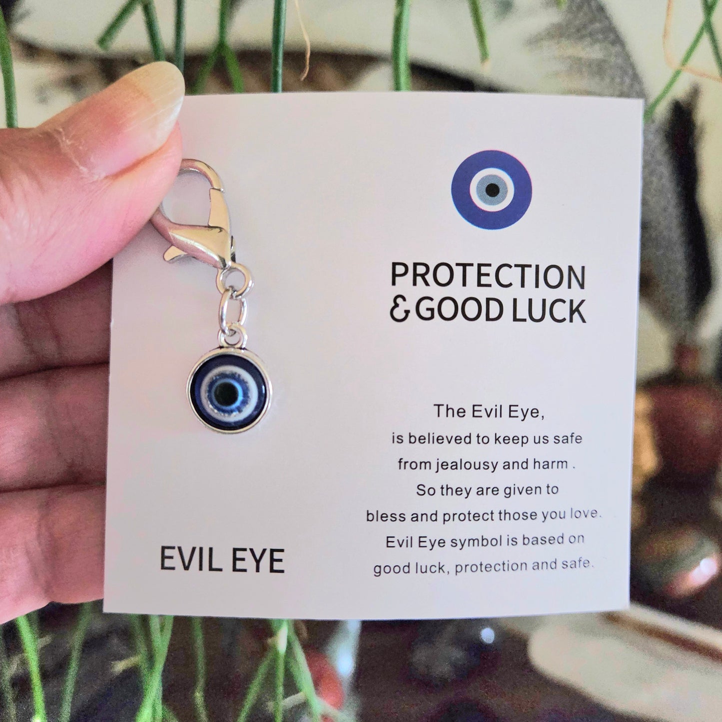 Evil eye charm on a card with text about protection and good luck, held by a hand.