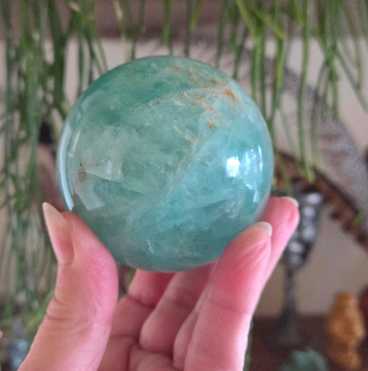 Hand holding a green crystal sphere with a blurred indoor background