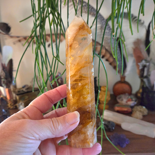 Hand holding a large crystal with a blurred background of decorative items and plants