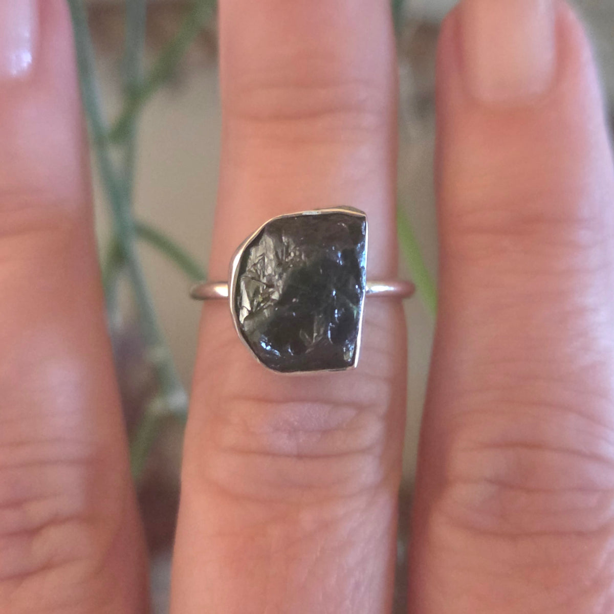 Silver ring with a large black stone on a finger against a blurred natural background