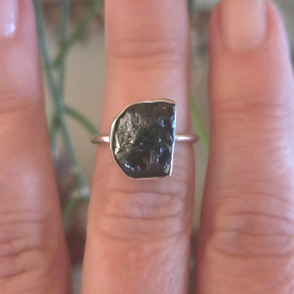 Silver ring with a large black stone on a finger against a blurred natural background