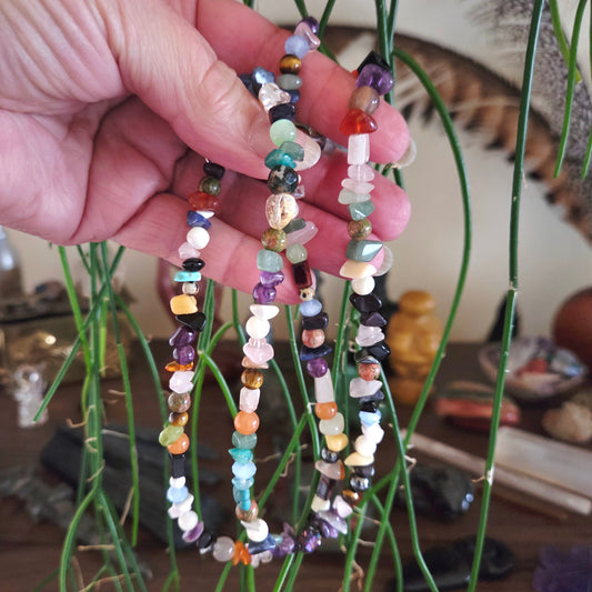 Hand holding three colorful beaded necklaces with a blurred indoor background