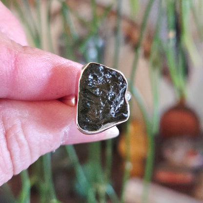 Hand holding a ring with a large, rough-cut gemstone against a blurred natural background