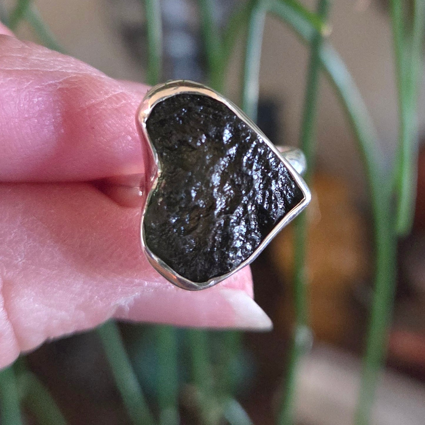 Silver ring with a dark stone held between fingers against a blurred background