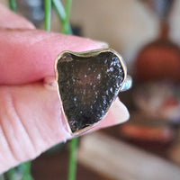 Close-up of a hand holding a ring with a dark stone and gold band.