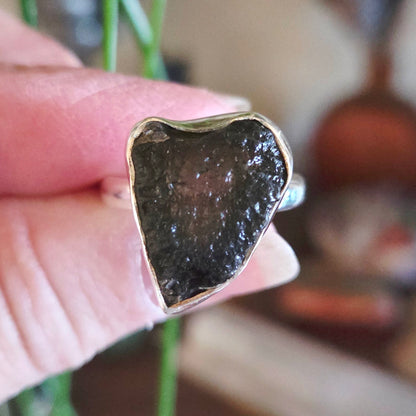 Close-up of a hand holding a ring with a dark stone and gold band.