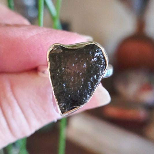 Close-up of a hand holding a ring with a dark stone and gold band.