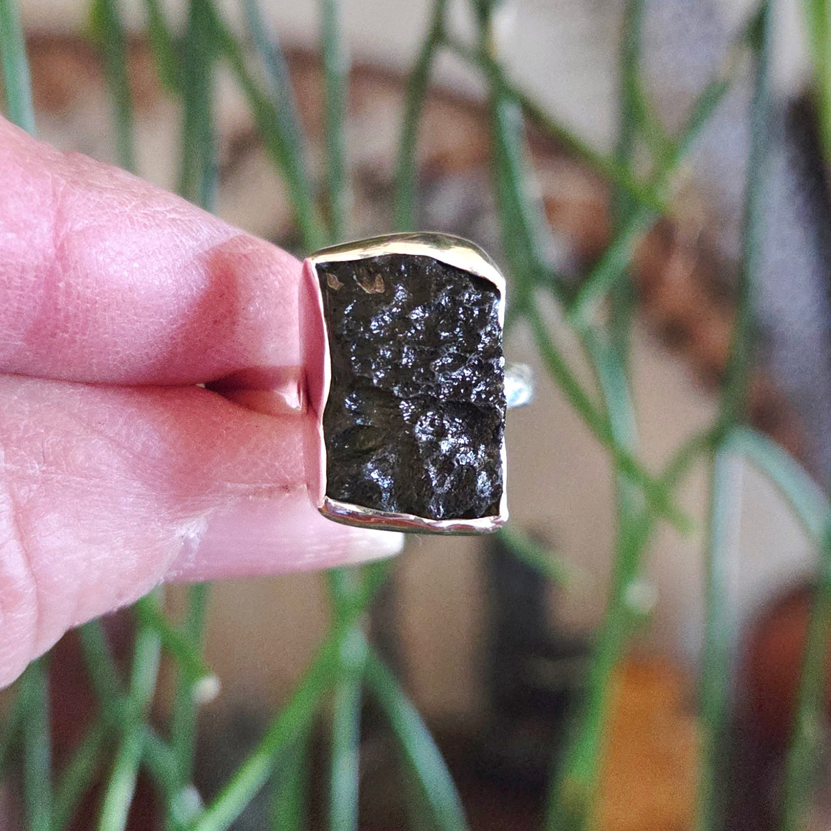 Ring with a dark stone held between fingers against a blurred background