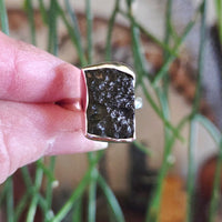 Ring with a dark stone held between fingers against a blurred background