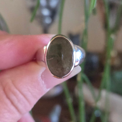 Silver ring with a green stone held by a hand against a blurred plant background