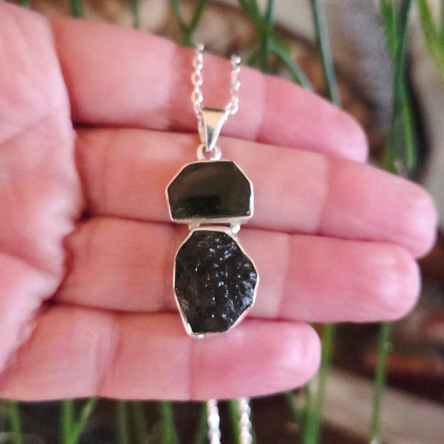 Necklace with a pendant held in a hand against a blurred natural background