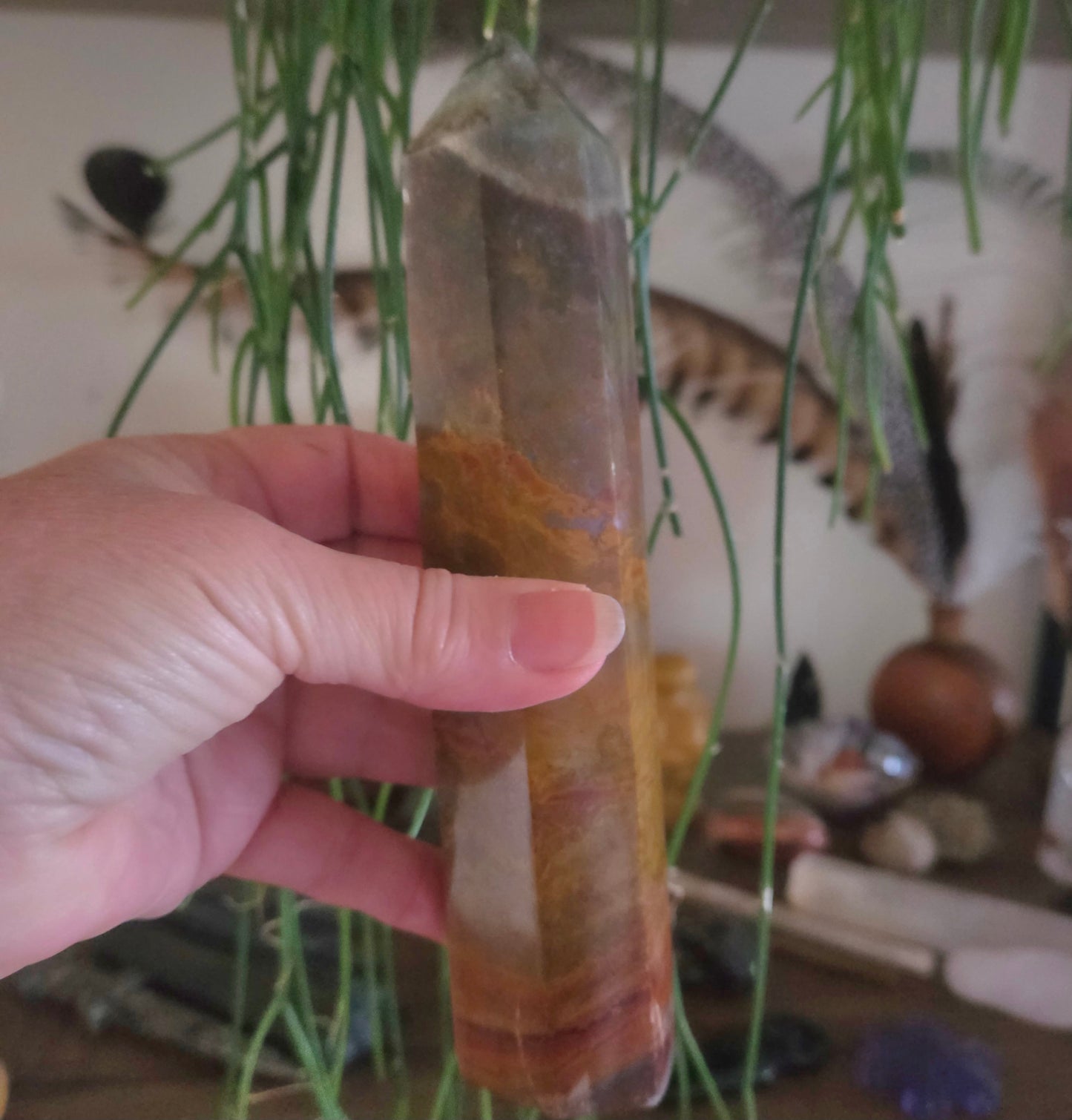 Hand holding a crystal with a blurred background of plants and decorative items