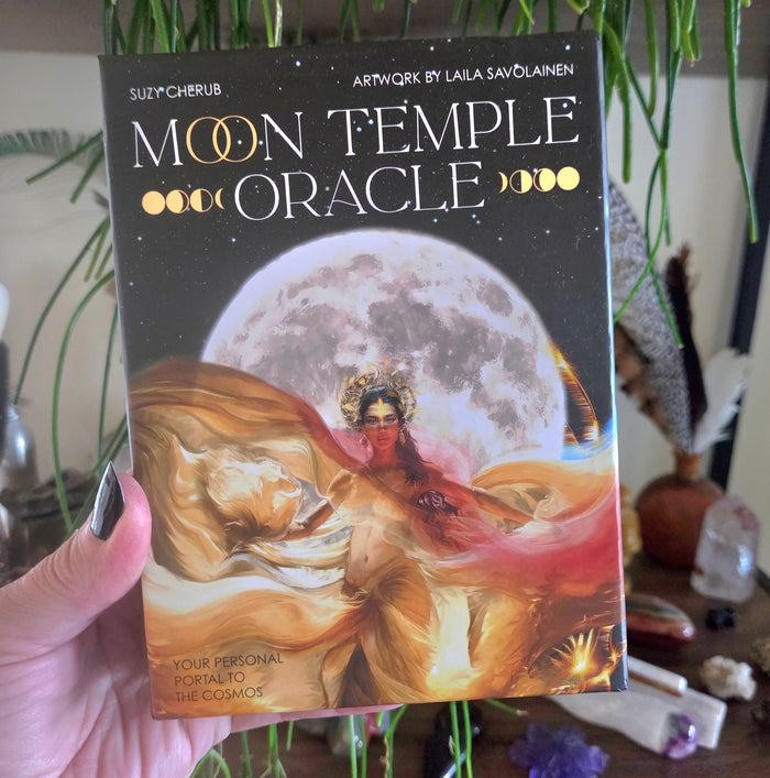 Book titled 'Moon Temple Oracle' held by a hand with a blurred background