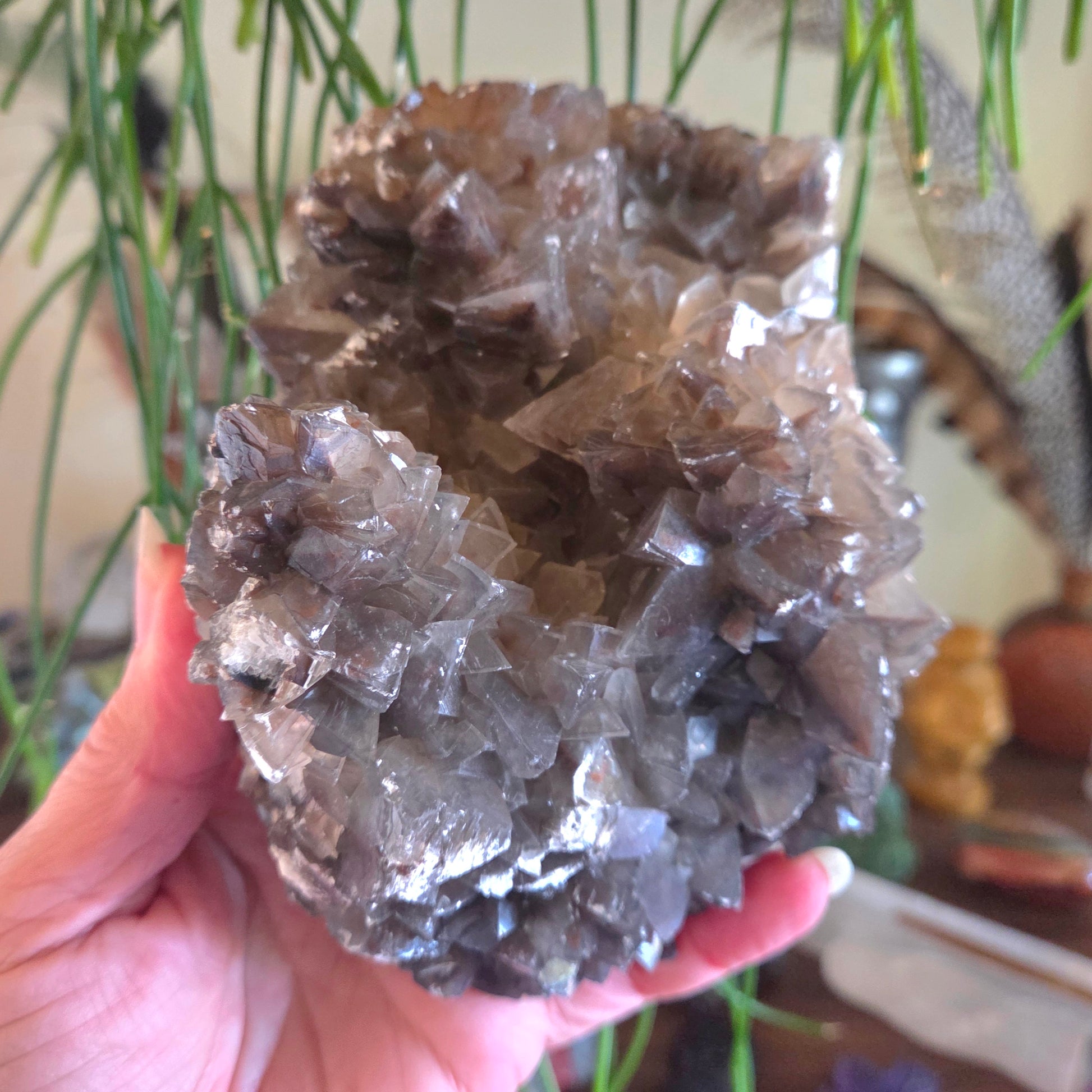 Hand holding a large crystal cluster with a blurred indoor background