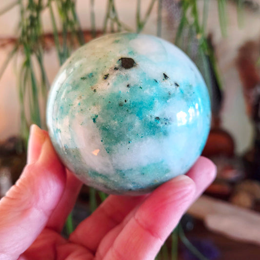 Hand holding a marbled blue and white sphere with a blurred natural background