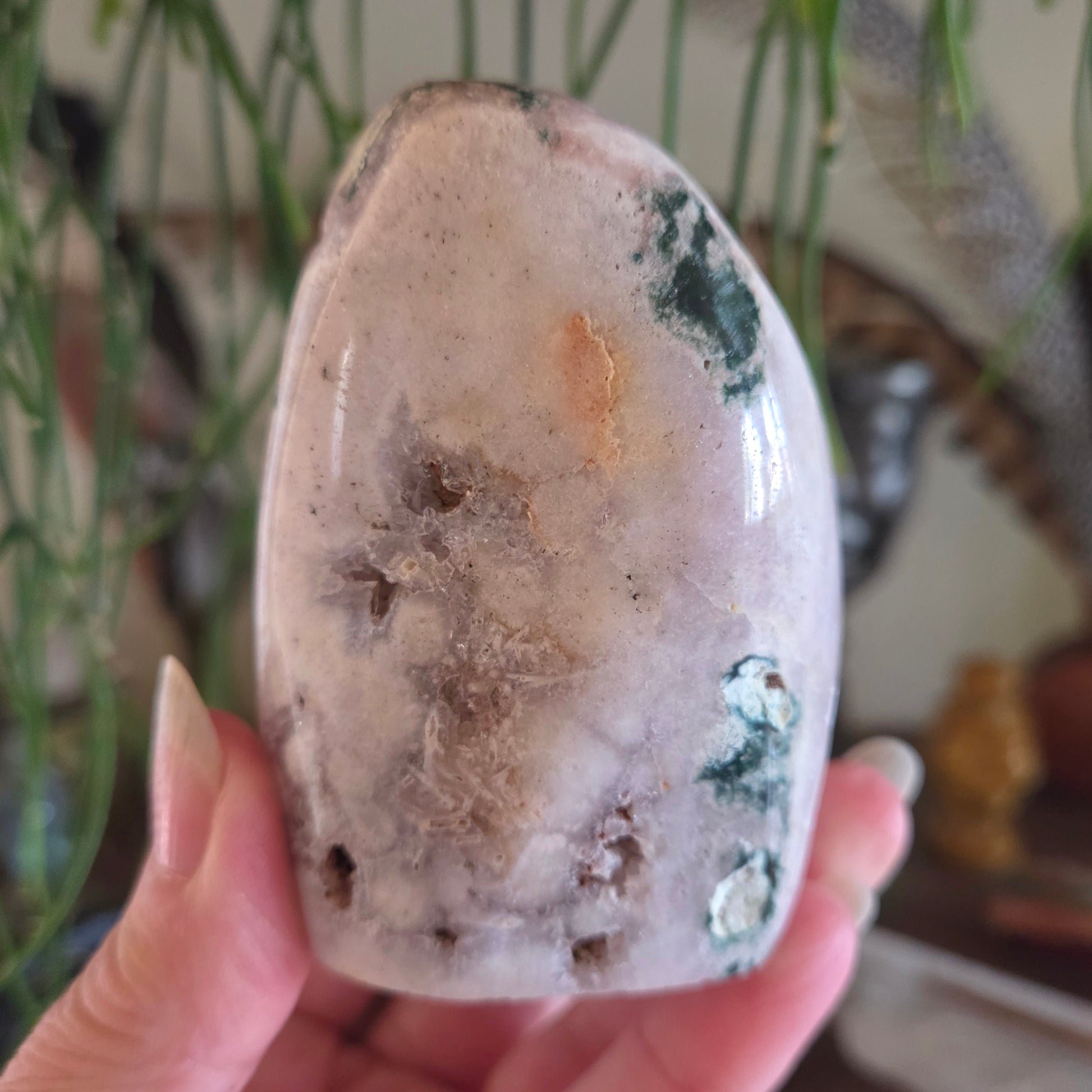 Hand holding a polished stone with natural patterns against a blurred indoor background