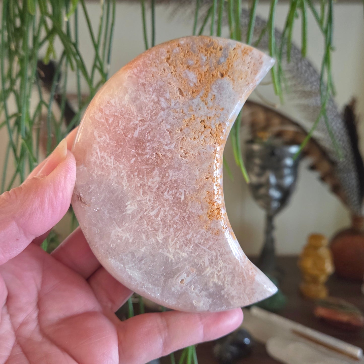 Hand holding a semi-circular stone with a natural texture and color, against a blurred indoor background.