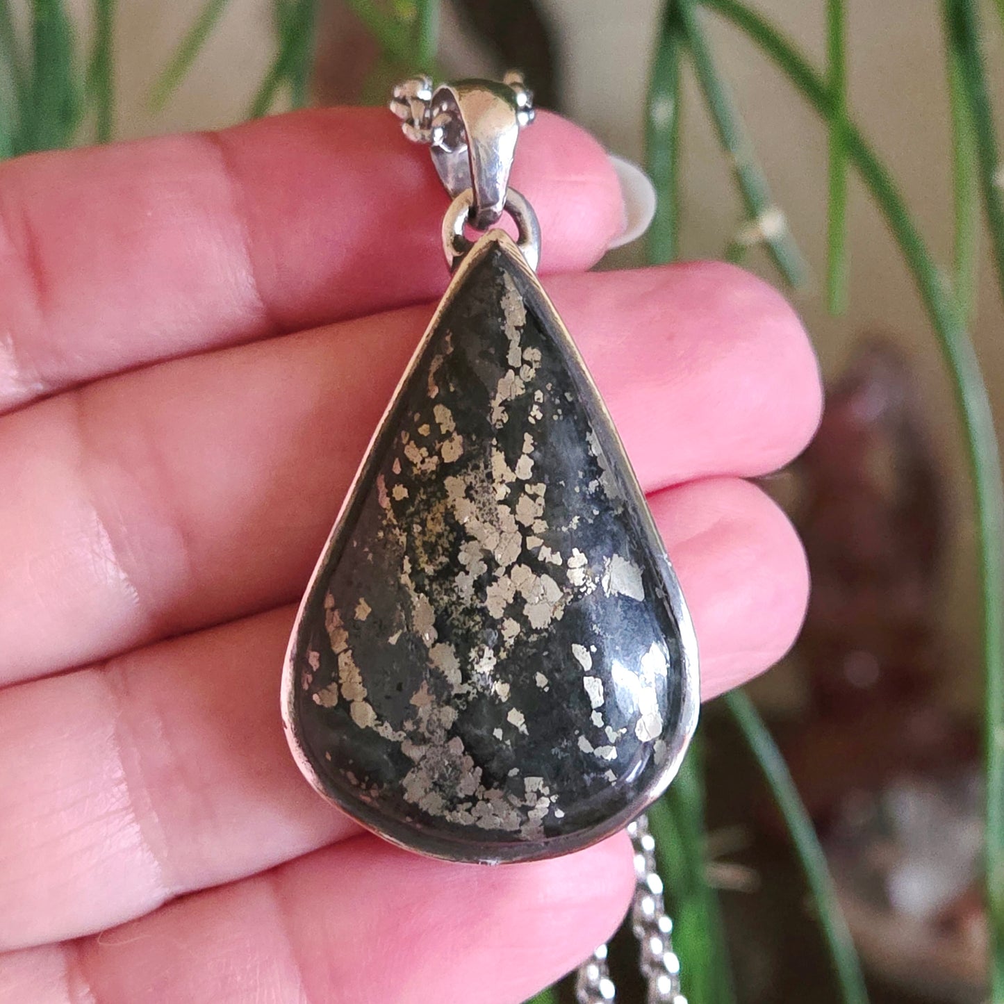 Teardrop-shaped pendant with speckled design held in a hand against a blurred natural background