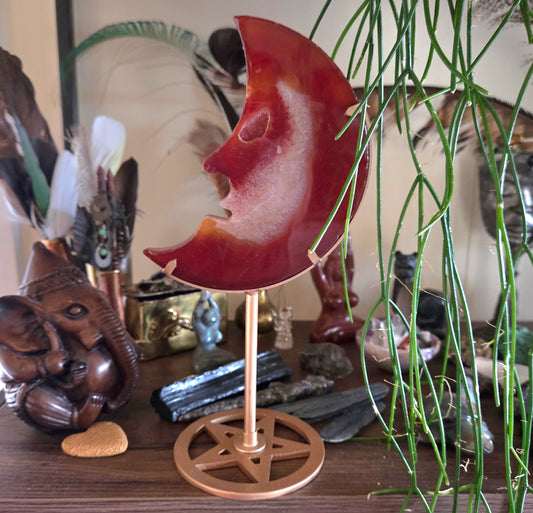 Decorative moon-shaped object on a stand with a wooden figure and plants in the background