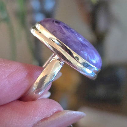 Ring with a purple stone held in a hand against a blurred background