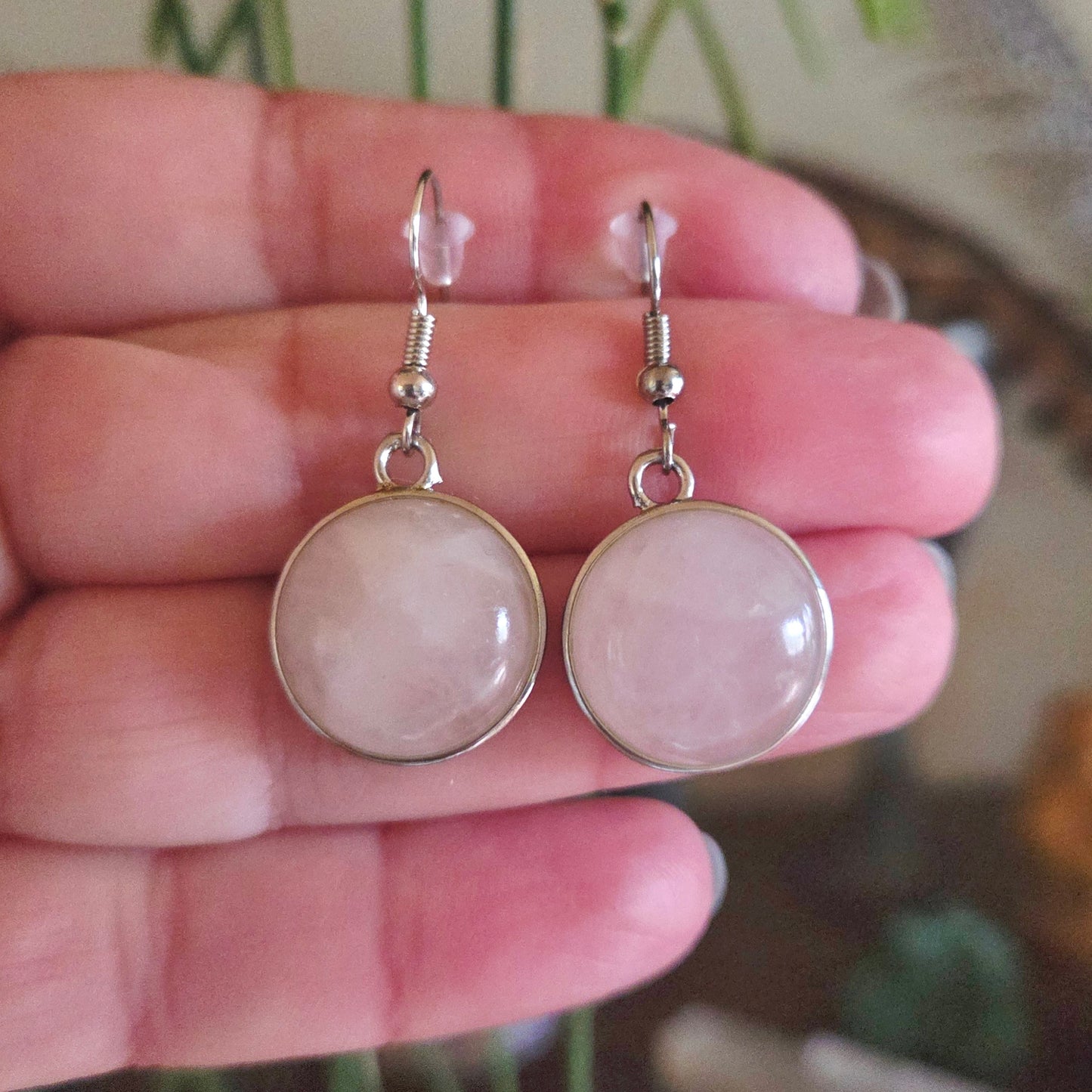Pink gemstone earrings held in a hand with a blurred background