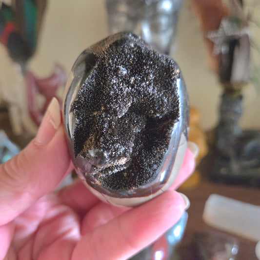 Hand holding a crystal with black and white patterns against a blurred background