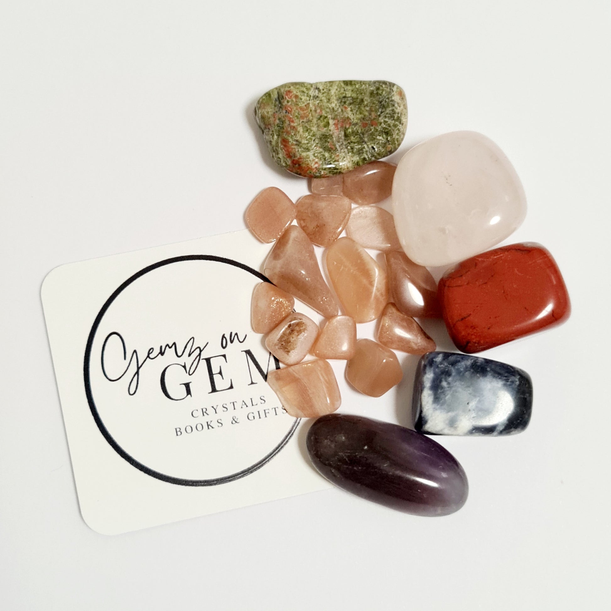 A collection of polished gemstones including pink, red, and clear varieties, displayed on a white card with 'Gemz on Gem' printed on it.