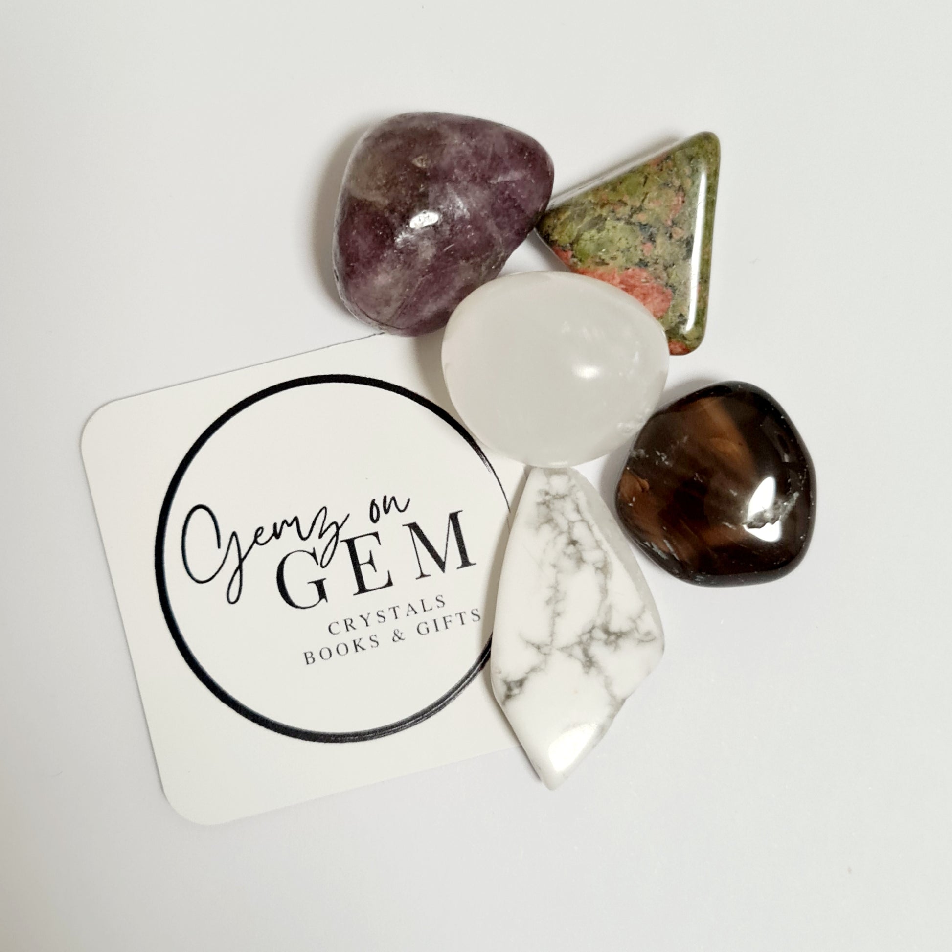 A collection of various crystal stones and decorative items on a white surface with a round label that reads 'Gemz on Gem'.