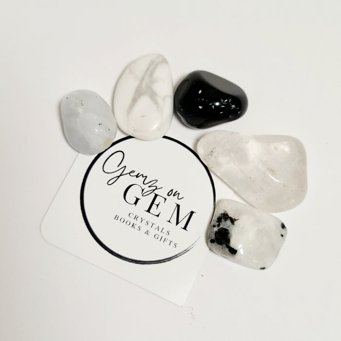 An assortment of polished crystals including a moonstone, a howlite, a blue calcite, an obsidian, and a clear quartz, displayed on a card with 'GEMZ ON GEM' branding.