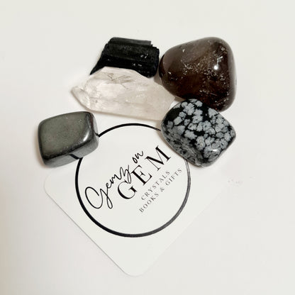 An assortment of polished crystals including black tourmaline, smoky quartz, hematite, and snowflake obsidian, displayed on a branded card with 'Gemz on Gem' printed on it.
