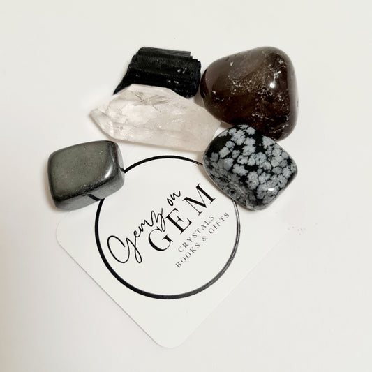 An assortment of polished crystals including black tourmaline, smoky quartz, hematite, and snowflake obsidian, displayed on a branded card with 'Gemz on Gem' printed on it.