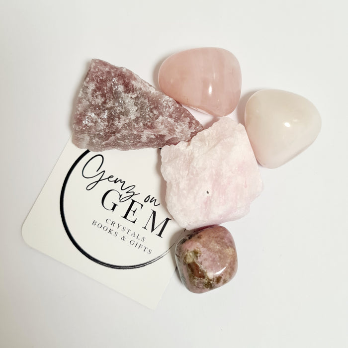 An assortment of pink and rose-colored crystals, including tumbled stones and raw crystal pieces, displayed on a branded card with 'Gemz on Gem' printed on it.