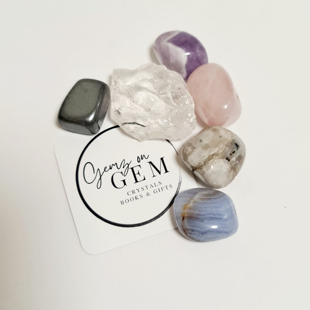 An assortment of polished gemstones including rose quartz, amethyst, blue lace agate, moonstone, and hematite, displayed on a card with 'Gemz on Gem' branding.
